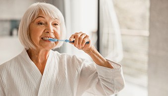 Woman smiling while brushing teeth in bathroom