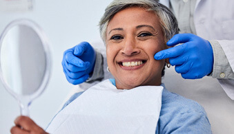 woman smiling and looking at her reflection in the dentist chair