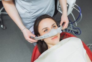 Woman with dark hair with eyes open while dentist places nitrous oxide mask